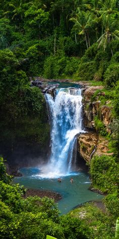 the waterfall is surrounded by lush green trees and blue water, while people are rafting in