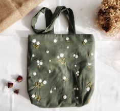 a green bag sitting on top of a bed next to a flowery plant and some dried flowers