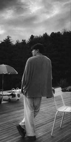 a man walking across a wooden deck next to a white chair and an open umbrella