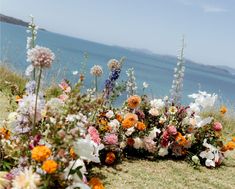 an arrangement of flowers on the side of a hill by the water's edge