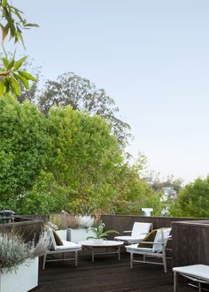 a wooden deck with white chairs and plants on the top floor, surrounded by greenery