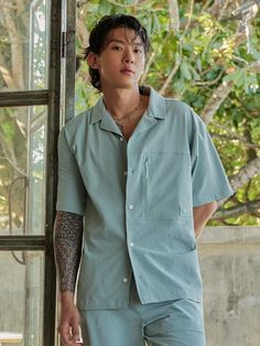 a man with tattoos standing in front of a window wearing a blue shirt and pants