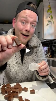 a man in a black hat is cutting up some chocolate squares on a counter top