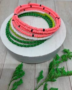 four bracelets on a white plate with green and pink bead trimming around them