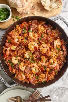 a skillet filled with shrimp and rice on top of a table next to bread