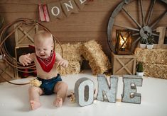 a baby is sitting on the floor in front of hay and letters that spell out one