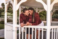 a man and woman hugging each other while standing on a white gazebo with trees in the background