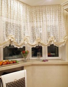 a kitchen window with white lace curtains and fruit on the counter in front of it