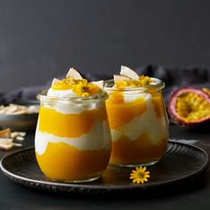 two glasses filled with dessert sitting on top of a black plate next to a pomegranate