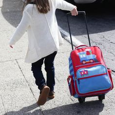 a woman walking down the street with her suitcase and handbag on wheels, pulling it behind her