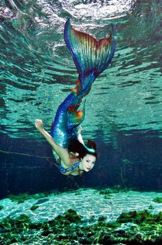 a woman is swimming under the water in a blue mermaid costume with her tail up