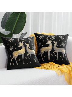 two black and gold deer pillows sitting on a white couch next to a green plant