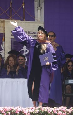 a woman in a graduation gown waves to the crowd