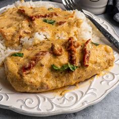 two pieces of meat covered in sauce and rice on a plate next to a fork