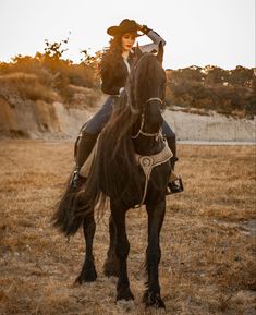 a woman riding on the back of a black horse in a grassy field at sunset