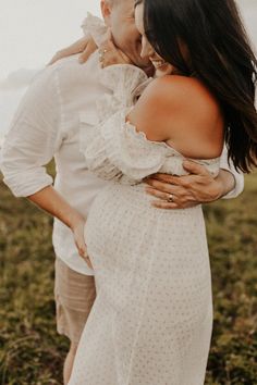 an older man and woman embracing each other in a field with mountains in the background