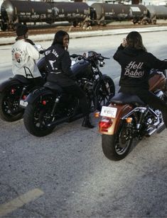 three people riding motorcycles on the road next to train tracks and railroad cars in the background