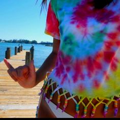 a woman is standing on a dock with her hand in her pocket and wearing a tie dye shirt