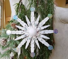 a white snowflake hanging from a tree with pine cones and ornaments around it