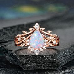 an opal and diamond ring is shown on top of a black rock with white stones