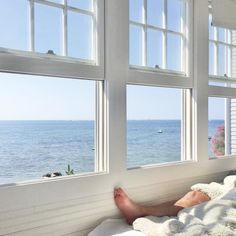 a person laying on a bed looking out the window at the ocean and boats in the water