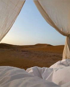 a bed with white sheets in the middle of a desert area and sand dunes behind it