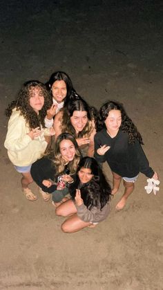 a group of young women sitting next to each other on top of a sandy beach