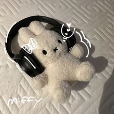 a white teddy bear with headphones on it's face sitting on a bed