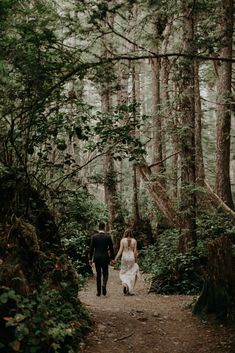 a bride and groom walking through the woods