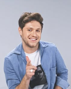 a young man is smiling and giving the thumbs up sign with his right hand while wearing a blue shirt