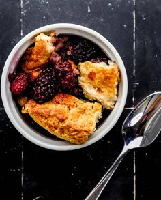 a bowl filled with fruit and bread on top of a wooden table next to a spoon