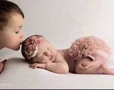 two babies laying next to each other on a white surface with their heads touching noses