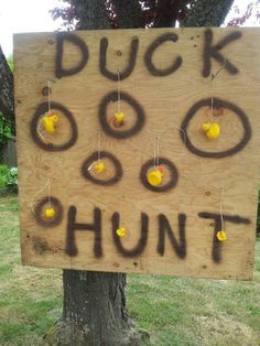 a wooden sign that says duck hunt hanging on a tree in the grass with yellow balls attached to it