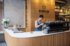 a person standing at a counter with a coffee maker in front of it and another person behind the counter