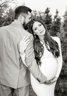 a man and woman are standing next to each other in front of some pine trees