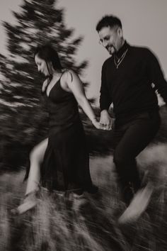 black and white photograph of man and woman holding each other's hands as they run through the grass