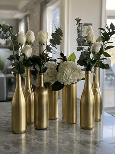 four gold vases with white flowers and greenery in them on a marble countertop