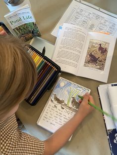 a little boy that is sitting at a table with some books and pencils in front of him