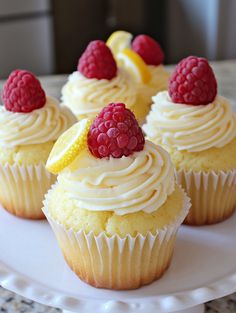 cupcakes with white frosting and raspberries on top are sitting on a plate