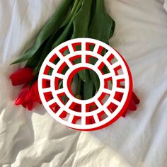 red tulips and green leaves laying on a white sheet with a circular cutout in the middle