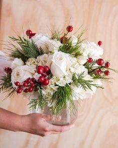 a bouquet of white roses and greenery is held by a woman's hand