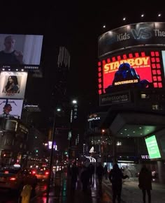 people are walking on the sidewalk in front of a building at night with lights and billboards