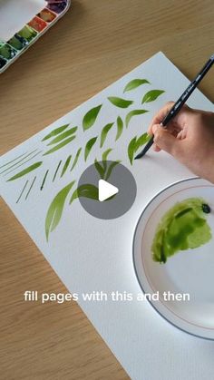 a person is painting on paper with green leaves and then using a brush to paint it