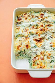 a casserole dish with cheese and spinach in it on an orange table