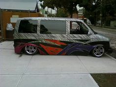 a van with flames painted on it parked in front of a fenced driveway area