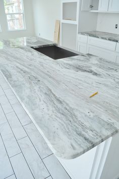 an empty kitchen with white cabinets and marble counter tops