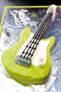 a cake shaped like an electric guitar on tin foil with green icing and white frosting