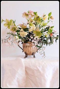 a vase filled with lots of flowers on top of a white cloth covered tablecloth