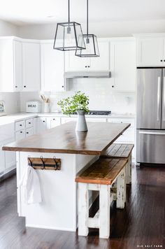 a kitchen with white cabinets and wooden counter tops, an island in front of the refrigerator