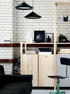 a living room filled with furniture next to a white brick wall covered in black hanging lights